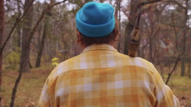 髭を生やした木こりが秋の森を歩き 斧を肩に担いで歩く ミッドショット — ストック動画