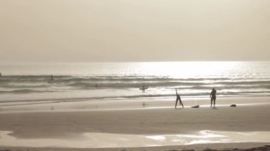 People surfing in the ocean - a woman warming up on the beach before going into the water. Mid shot