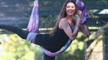 Smiling woman having fun while doing aerial yoga. Mid shot