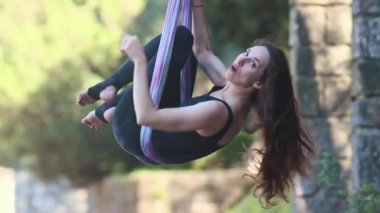 A woman with long hair hanging in yoga hammock and talking. Mid shot