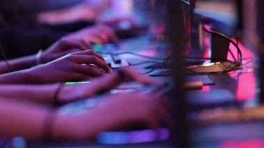 Young men sit and play online games in neon lighting at competition. Mid shot