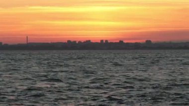 The city is on the horizon and the sea is agitated at sunset. Mid shot