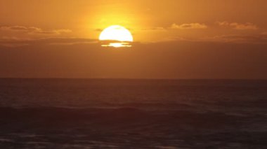 Big orange sun sets behind the clouds over the sea. Mid shot