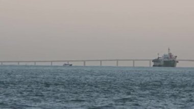 An industrial marine vessel sails the river and the motor boat is floating nearby. Mid shot