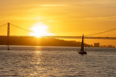 Bright orange sunset over the river and a sailing boat floating towards the bridge. Mid shot