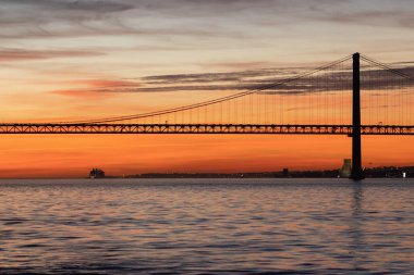 Lisbon and 25th of April Bridge at orange sunset. Mid shot
