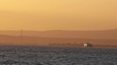 A boat floats down the river at muddy orange sunset. Mid shot