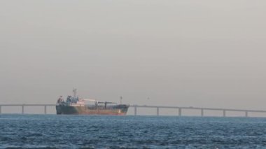 An old industrial mining vessel sails down a river against the backdrop of a bridge. Mid shot