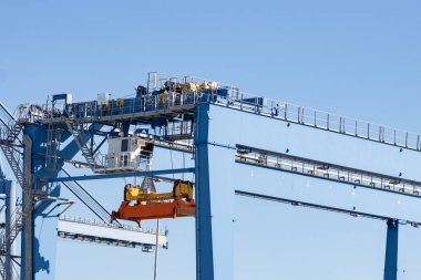 Large lifting structures with suspended spreader for cargo containers on the background of the blue sky. Mid shot