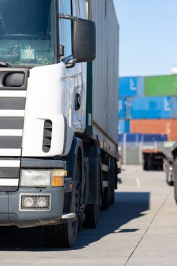 A truck stands at the seaport with colored cargo containers on the background. Mid shot