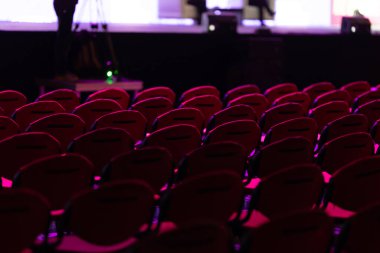 Rows of red chairs in an empty hall. Mid shot