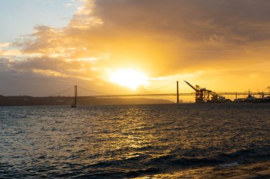 Sunset over the sea and silhouettes of a bridge and an industrial crane. Mid shot