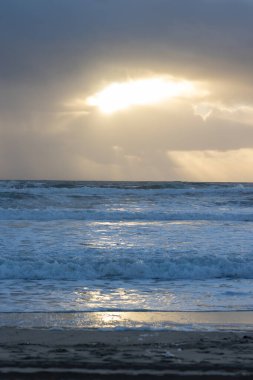 Sea waves and bright light breaking through the clouds in the sky. Vertical shot