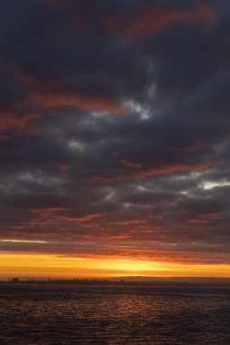Bright orange sunset and thick clouds above the sea. Vertical shot