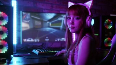 Cute gamer girl sitting by PC and looks in the camera. Mid shot