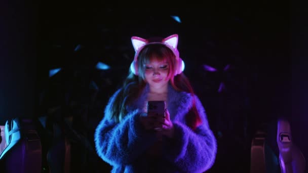 Симпатичная Девушка Геймер Наушниках Светящимися Кошачьими Ушами Использует Свой Телефон — стоковое видео