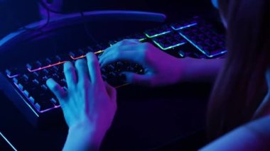 Gamer girl tapping on her neon backlit keyboard. Mid shot