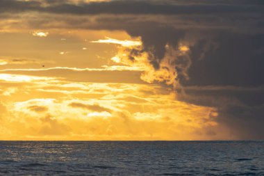 Bright and cloudy yellow sunset over the dark sea. Mid shot