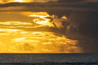 Bright and cloudy yellow sunset over the dark blue sea. Mid shot