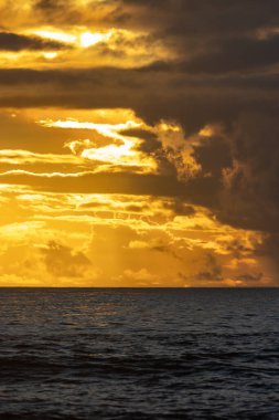 Cloudy yellow sunset over the dark sea. Vertical shot