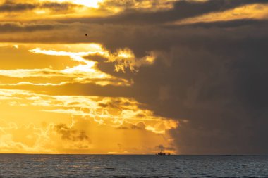 Landscape of bright yellow sunset sky over the dark sea - a boat sails in the distance. Mid shot