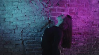 Güzel bir kadın dansçı, neon ışıkta, tuğla bir duvara karşı seksi siyah elbiseler içinde. Orta çekim