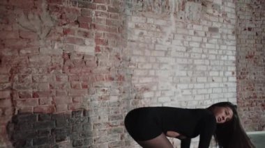 An attractive woman in a sexy black outfit bending back standing by the brick wall. Mid shot