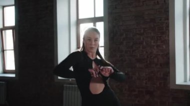 Attractive woman dancer with long natural hair and wearing sexy black outfit dances in the studio. Mid shot