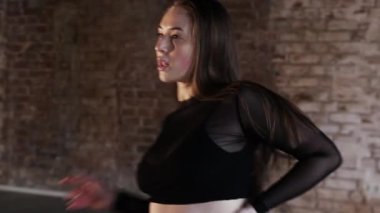 Pretty woman with nice body dancing in the studio with brick walls. Mid shot