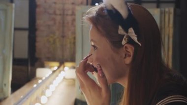 A young pretty woman cosplayer blending in foundation on her face using a sponge - looking in a backstage mirror. Mid shot