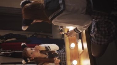 A cute girl doing makeup in front of a mirror at the backstage. Vertical shot