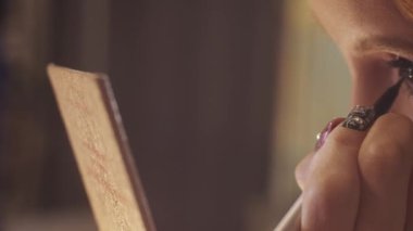 A cute young woman doing makeup - drawing dramatic winged eyeliner. Close up