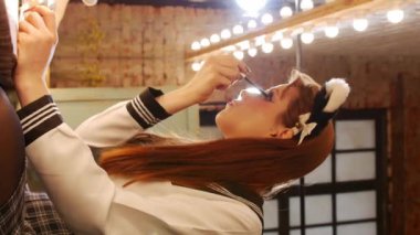 A cute girl doing makeup - applying mascara to her eyelashes sitting in front of a mirror. Vertical shot