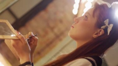 A cute girl doing heavy eye makeup. Mid shot
