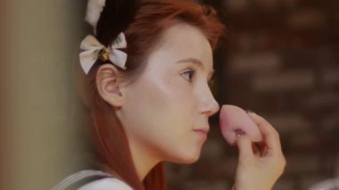 A cute girl cosplayer doing makeup - blending in highlighter on her cheekbones using a sponge. Mid shot