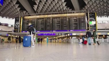 22-01-2023 Frankfurt, Germany: Departure scoreboard at the airport and people passing by. Time-lapse