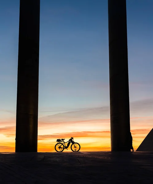 The bike stands at sunset between two columns. Vertical shot