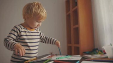 Cute little blonde boy drawing with color pencils. Mid shot