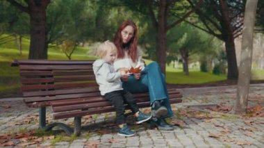 Woman with her little son in the park - little boy collecting autumn leaves. Mid shot