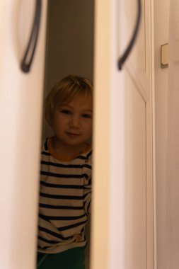 Cute little blonde boy hiding in a closet. Vertical shot