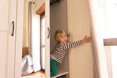 Cute little boy sitting in the closet. Mid shot