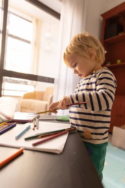 Cute little blonde boy playing with color pencils. Vertical shot