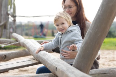 A mother wearing glasses with her cute smiling little son on the playground. Mid shot
