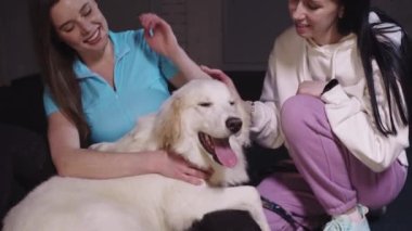 Two smiling young women petting a cute white dog. Vertical shot