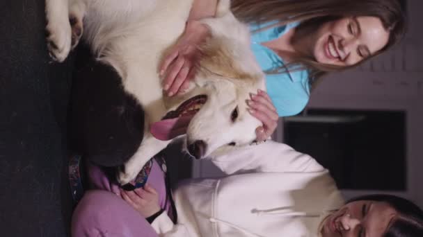Two Young Women Petting Cute White Dog Vertical Shot — стоковое видео