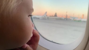 Uçakta oturan pencereye bakan küçük sarışın bir çocuk. Portre