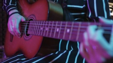 Stüdyoda renkli ışıkta gitar çalan genç bir kadın. Orta çekim