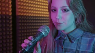 Kanatlı göz kalemi kullanan güzel bir kadın kameraya yaklaştı ve mikrofonda şarkı söylemeye başladı. Portre