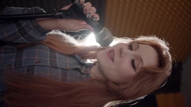 一个年轻的女人在录音室里录制一首歌 一边用麦克风唱歌 一边看着摄像机 垂直射击 — 图库视频影像