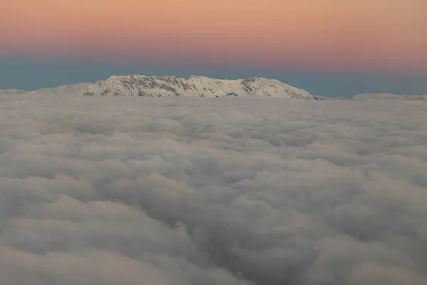 Peaks of snowy mountains over gray clouds in the dawn sky. Mid shot